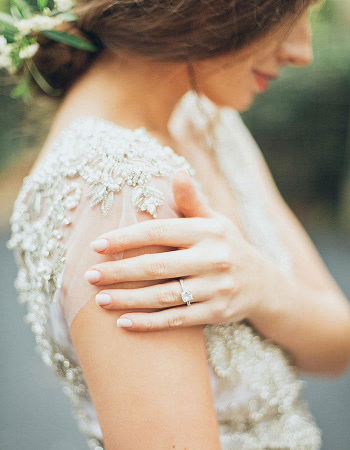 Close-up of a person wearing a round engagement ring in a delicate white lace garment with floral details.