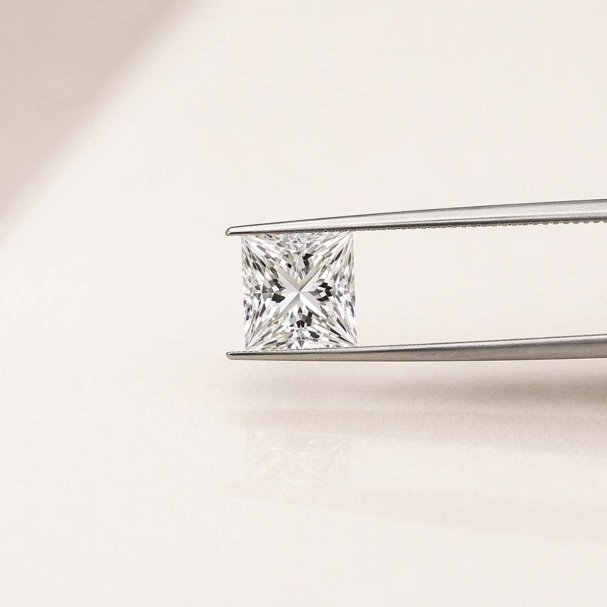 A princess-cut diamond held in the jaws of silver tweezers against a clean, light beige background.