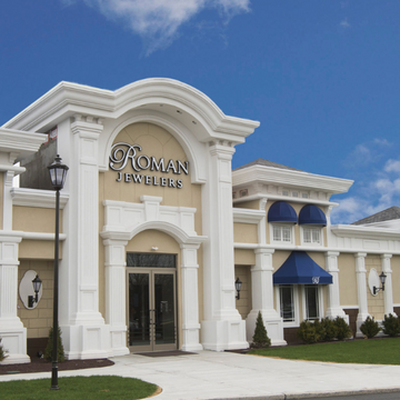 The exterior of Roman Jewelers in Bridgewater, New Jersey. A white and cream elegant building with blue awnings against a blue sky