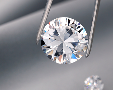 Round diamond held by tweezers against a gray background